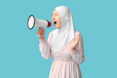 Genç Asyalı Müslüman kadın mavi arka planda megafona bağırıyor. Ulusal Duyulma Günü