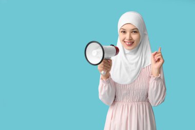 Mavi arka plandaki bir şeyi işaret eden megafonlu genç Asyalı Müslüman kadın. Ulusal Duyulma Günü