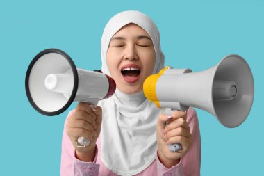 Genç Asyalı Müslüman kadın mavi arka planda megafonlara bağırıyor. Ulusal Duyulma Günü