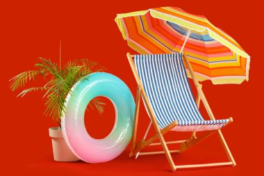 Güverte sandalyesi, plaj şemsiyesi, şişirilebilir yüzük ve kırmızı arka planda egzotik bitki.