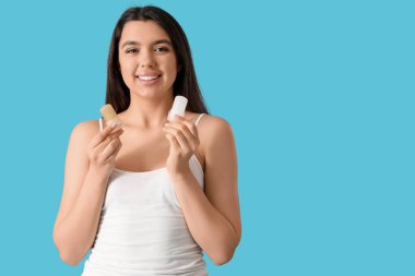 Mavi arka planda kristal deodorantları olan mutlu genç bir kadın.