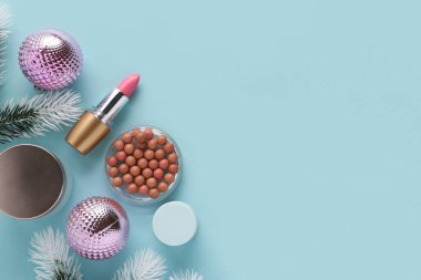 Noel toplarıyla dekoratif kozmetik ürünleri ve mavi arka planda köknar ağacı dalları. Üst görünüm
