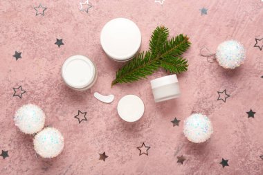 Kozmetik ürünlerin kavanozları, köknar dalı ve pembe grunge arka planında konfetisi olan güzel bir kompozisyon.