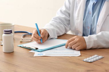 Steteskop yakınındaki panoya yazı yazan erkek doktor ve ahşap masada haplar.