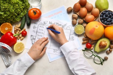 Kadın beslenme uzmanı masadaki sağlıklı yiyeceklerin yanında diyet planı yazıyor.