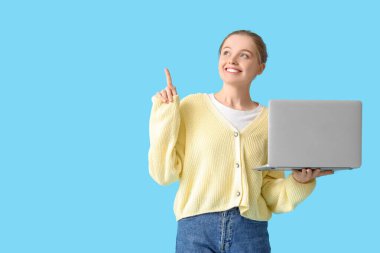 Modern dizüstü bilgisayarı olan genç bir kadın mavi arka planda bir şeye bakıyor.