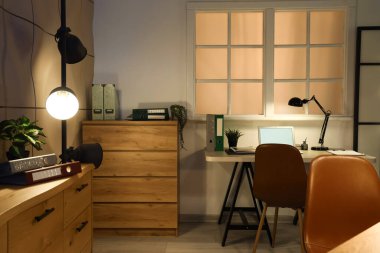 Çalışma odası, çekmeceler ve parlayan lambalar olan karanlık ofisin içinde.