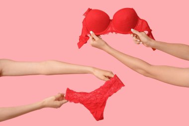 Pembe arka planda zarif dantel iç çamaşırlı kadın elleri, yakın plan.