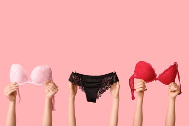 Pembe arka planda zarif dantel iç çamaşırlı kadın elleri, yakın plan.