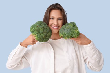 Mavi arka planda taze brokoli olan güzel, genç, mutlu bir kadın. Diyet kavramı