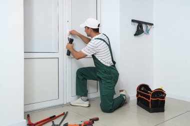 Ofis kapısını tamir eden elektrikli matkap kullanan bir erkek işçi.