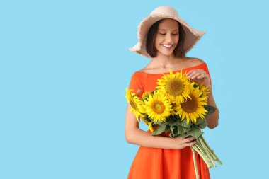 Hasır şapkalı, mavi arka planda bir buket ayçiçeği olan genç ve güzel bir kadın.