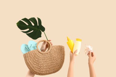 Güneş kremi, kabuk, çanta, canavar yaprağı ve bej arka planda parmak arası terlik olan kadın elleri. Seyahat kavramı