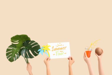 Kokteylli, hindistan cevizli, kağıt palmiye ağaçlı kadın elleri, yazı süresini gösteren kağıt ve bej arka planda canavar yaprakları. Seyahat kavramı