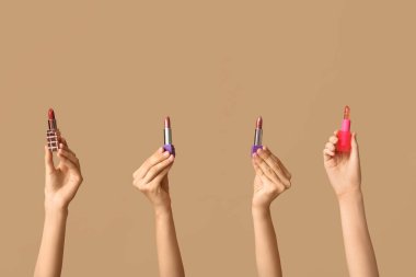 Kahverengi arka planda bir sürü ruju olan kadın elleri.