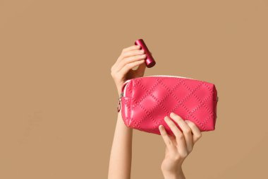 Kozmetik çantalı kadın elleri ve kahverengi arka planda ruj.