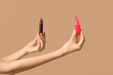 Kahverengi arka planda farklı ruj izleri olan kadın elleri.