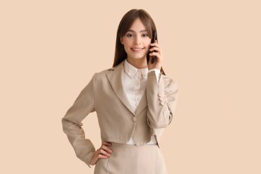 Güzel genç iş kadını bej arka planda cep telefonuyla konuşuyor.