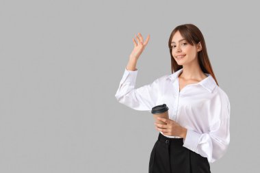 Gri arka planda bir fincan kahvesi olan genç ve güzel bir iş kadını.