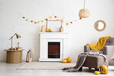 Modern şöminesi, koltuğu, masası ve sonbahar süslemeleri beyaz tuğla duvarın yanında.