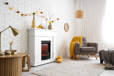 Modern şöminesi, koltuğu, masası ve sonbahar süslemeleri beyaz tuğla duvarın yanında.