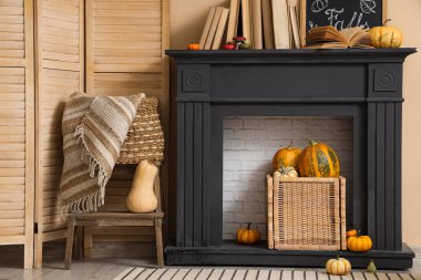 Bej duvarın yanındaki modern şöminede katlanan perdeli, kitaplı ve sonbahar dekorasyonlu şık bir oda.