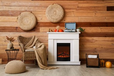 Hasır koltuğu, pikabı ve kahverengi ahşap duvarın yanındaki modern şöminede sonbahar süslemeleri olan şık bir oda.