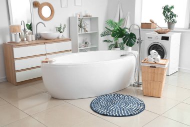 Yuvarlak paspası, çamaşır sepeti ve çamaşır makinesi olan banyonun içi.