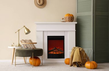 Beyaz şömineli, yumuşak puflu, balkabaklı ve kitaplı aydınlık oturma odasının içi.