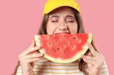 Güzel, genç, mutlu bir kadın pembe arka planda taze karpuz yiyor.