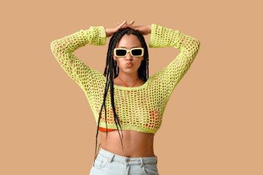 Havalı, bej arka planda örgüleri olan Afro-Amerikalı bir kadın.