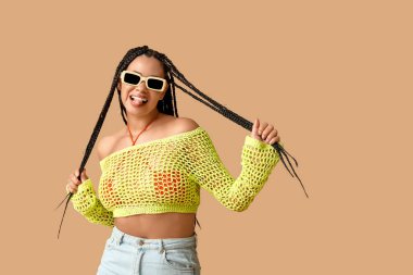 Havalı, bej arka planda örgüleri olan Afro-Amerikalı bir kadın.