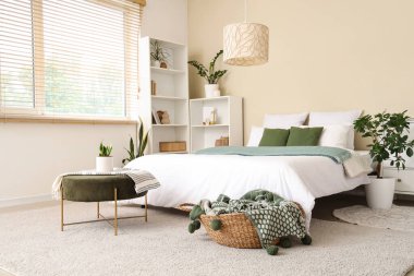 Rahat yatak, raf ünitesi, yatak odasının içinde ekoseli puf ve sepet.