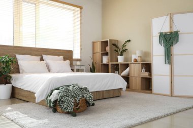 Rahat bir yatak, yatak odasının içinde ekoseli raf ve sepet.