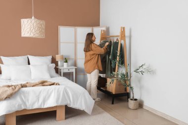 Güzel genç bayan modern yatak odasında kıyafet seçiyor.