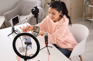 Female beauty blogger with eyeshadows recording video at home