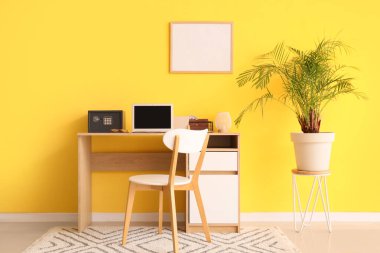 Modern bilgisayar ve kasa sarı duvarın yanındaki masada.