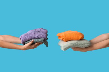 Mavi arka planda sıcak giysi yığını olan kadın elleri