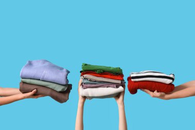 Mavi arka planda farklı giysi yığınları olan birçok kadın eli