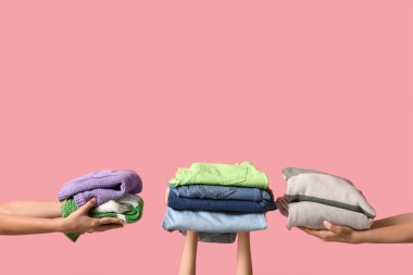 Pembe arka planda farklı giysi yığınları olan birçok kadın eli.