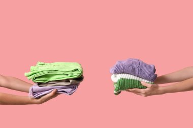 Pembe arka planda farklı giysi yığınları olan kadın elleri