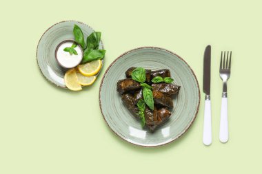 Lezzetli Dolmas tabakları (doldurulmuş üzüm yaprakları), limon dilimleri, ekşi krema ve renk arka planında çatal bıçak takımı