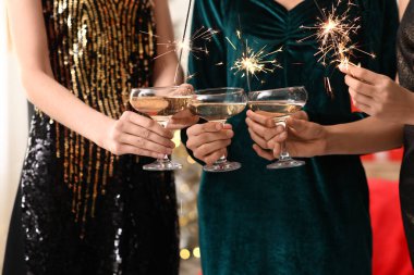 Yanan Noel havai fişekleri olan güzel elbiseli kadınlar şampanya içip, yakınlaşırlar.