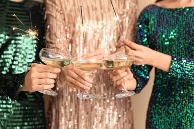 Şampanyalı zarif elbiseli kadınlar ve renkli arka planda yanan Noel maytapları, yakın plan.