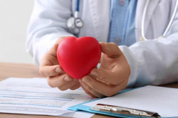 Женщина-врач держит красное сердце за столом в офисе. Концепция медицинского страхования