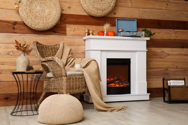 Hasır koltuğu, pikabı ve kahverengi ahşap duvarın yanındaki modern şöminede sonbahar süslemeleri olan şık bir oda.