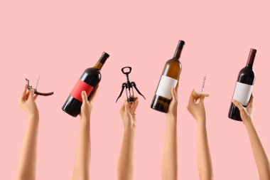 Pembe arka planda şarap şişeleri ve tirbuşon tutan kadın eller.