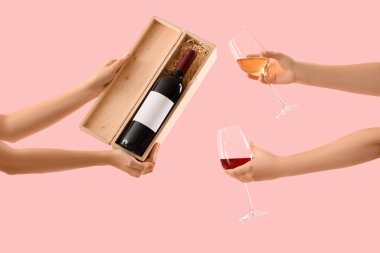 Pembe arka planda şarap şişesi ve gözlüklü kadın eller.