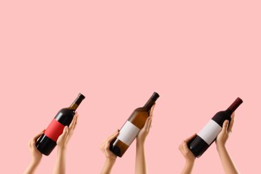 Pembe arka planda şarap şişelerini tutan kadın eller.