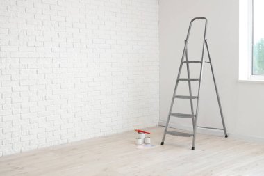 Beyaz duvarın yanında boya ve fırça dolu merdiven.